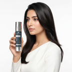 Woman holding a skincare serum bottle with a plain background