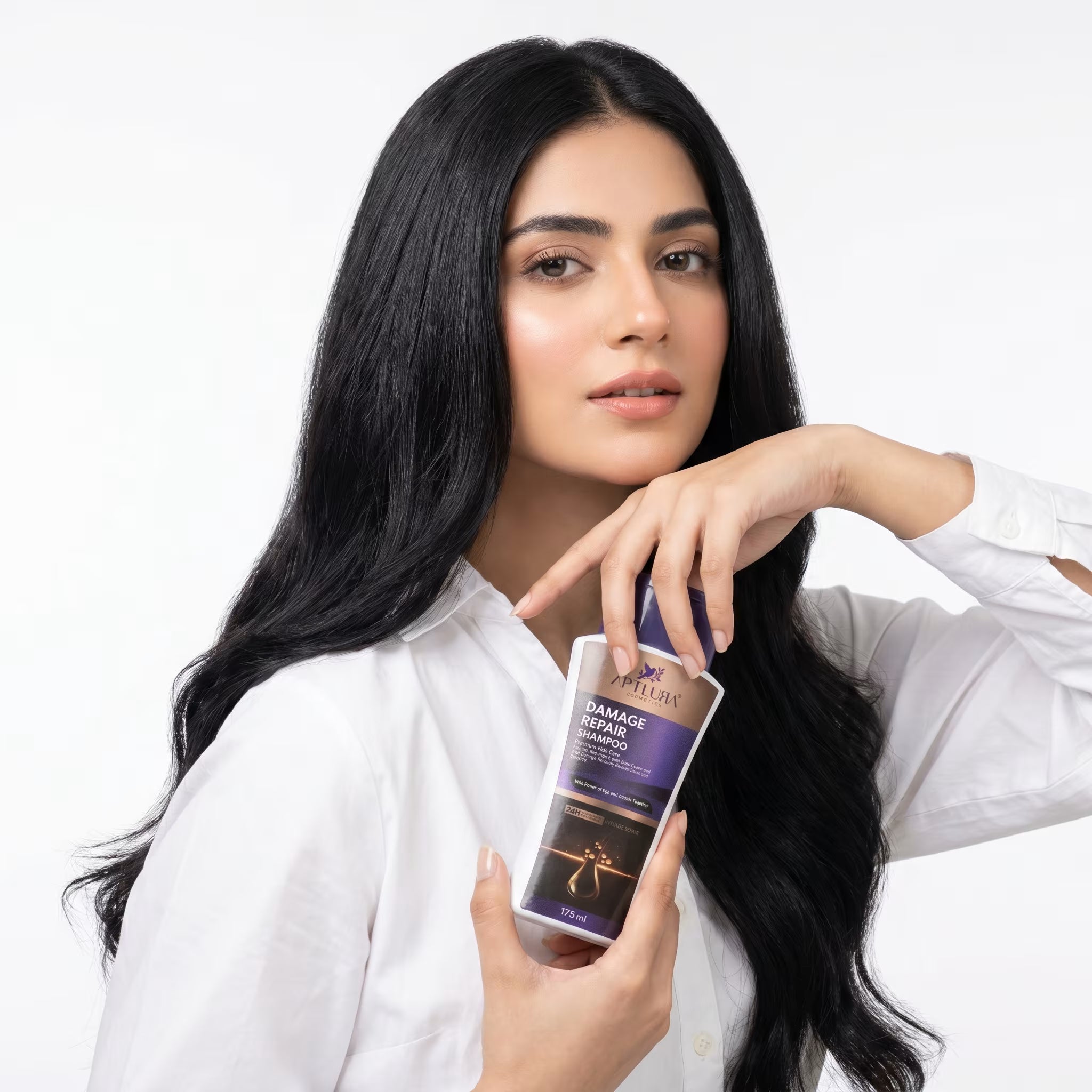 Woman with long black hair holding a bottle of shampoo against a white background