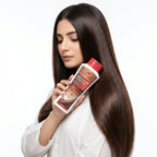 Woman with long brown hair holding a bottle of hair care product on a white background