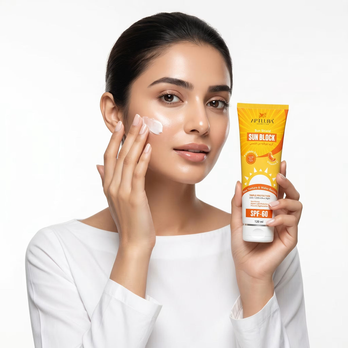 Woman applying sunscreen cream to her face with a tube of sunscreen in her other hand on a white background
