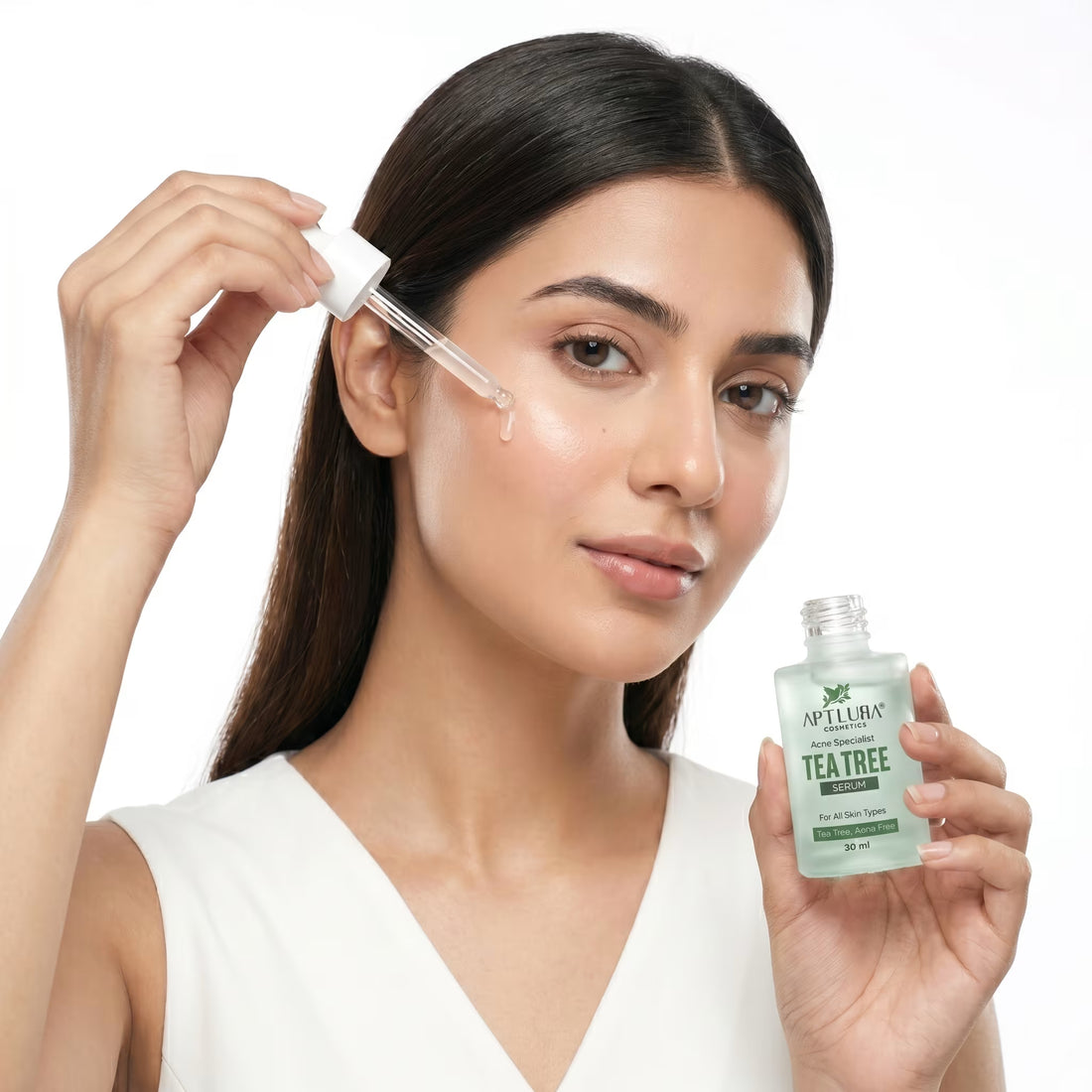 Woman applying tea tree oil to her face with a dropper, holding a bottle of Aptus Tea Tree oil.