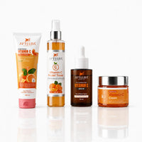 Four skincare products from Aptlura Cosmetics Vitamin C line arranged on a reflective white surface: a pink-and-white tube, an amber spray bottle, a dark brown dropper serum bottle, and an amber cream jar with silver lids.