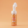 Foaming bubble wash bottle with orange label on a beige background