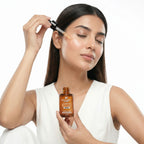 Woman applying a dropper of skincare product to her face with a bottle in hand on a white background