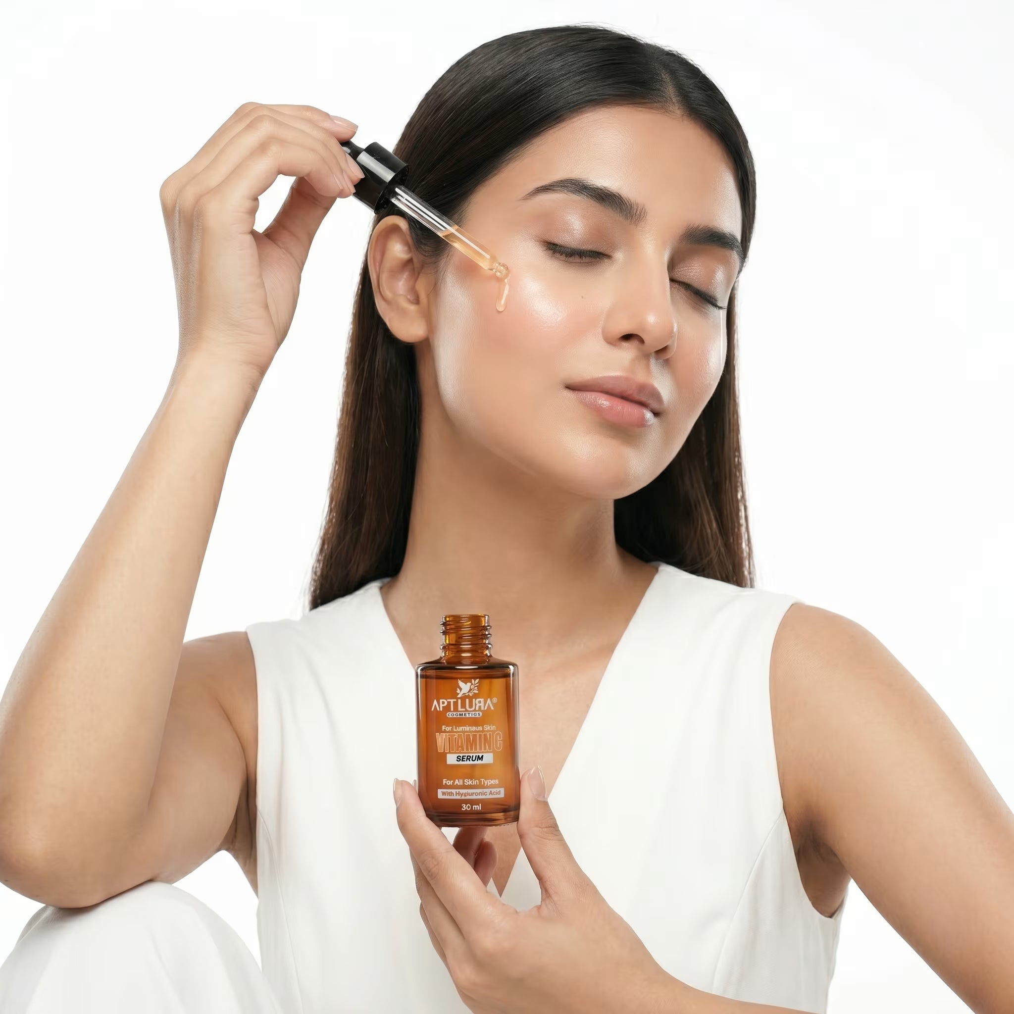 Woman applying a dropper of skincare product to her face with a bottle in hand on a white background